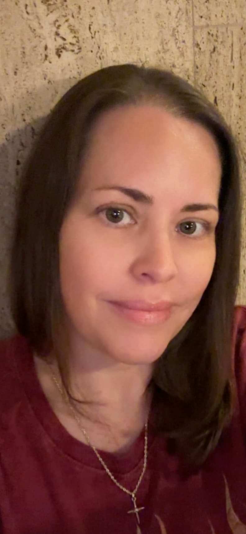 Woman with dark brown hair and eyes, wearing a maroon shirt and gold cross necklace.